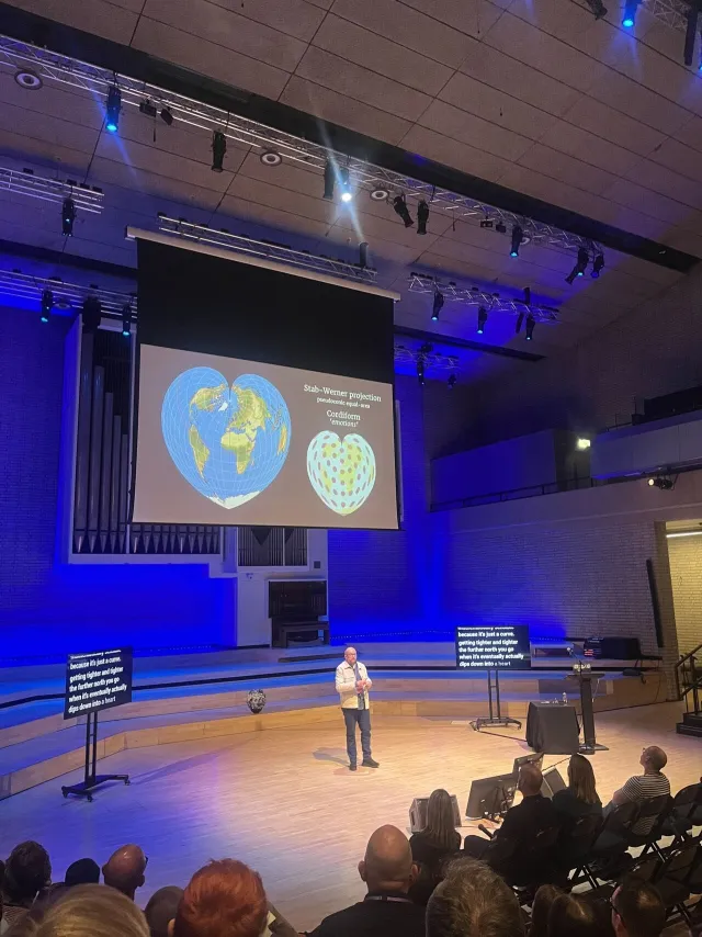 Foto: Megan L.: Per Axbom på scen på Camp Digital 2025. Jämförelse av hjärtformade kartprojektioner.