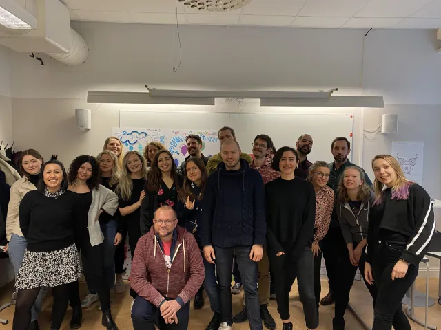 Per på knä framför en klass med ett tjugofemtal UX-studenter, alla leende, i ett klassrum med affischer på whiteboarden bakom dem, februari 2020.