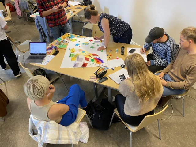 Grupparbete, september 2022: Studenter runt bord täckta av papper, färgpennor och lappar, i arbete med en stor affisch.